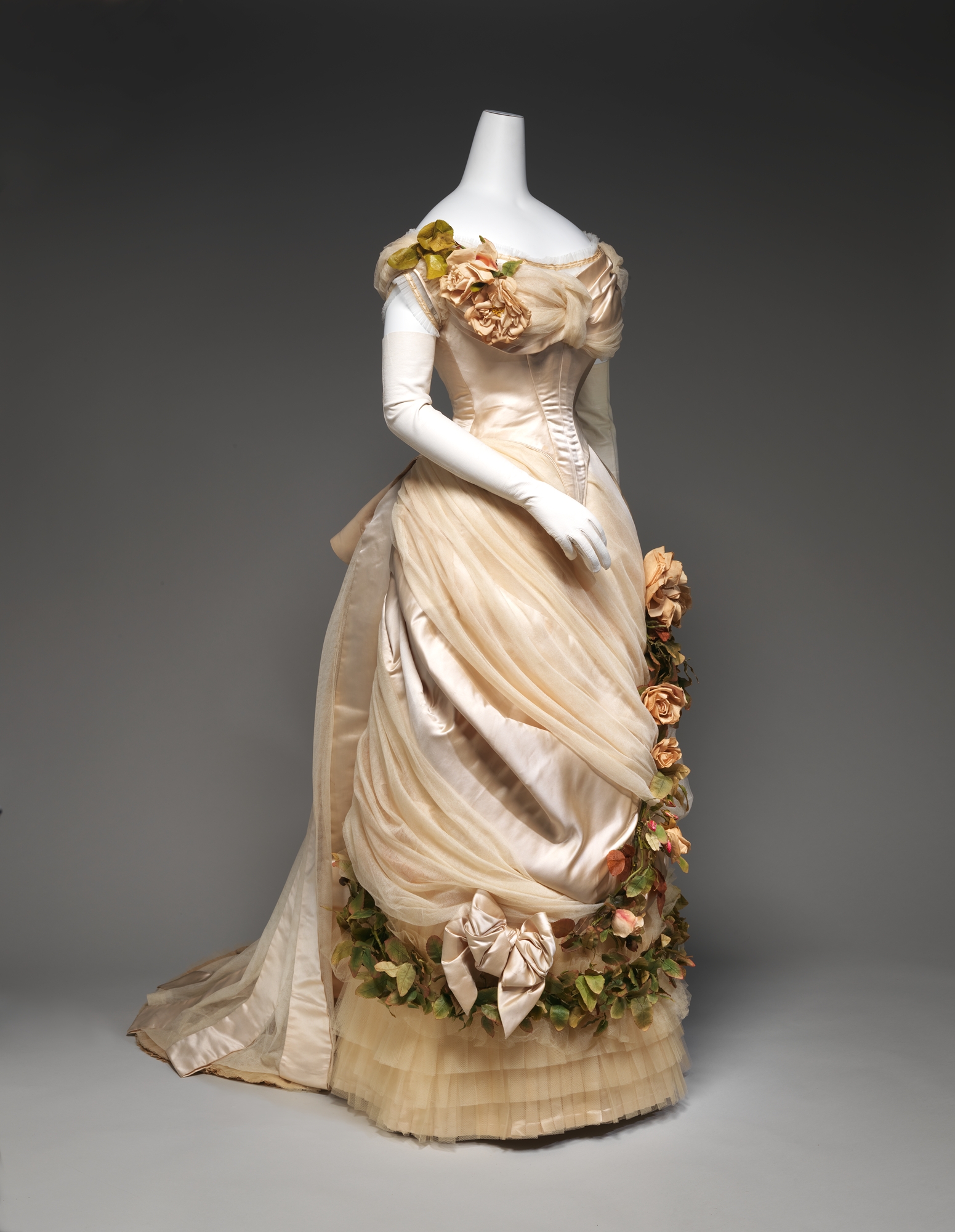 Ivory and blue silk evening dress with a fitted bodice, deep neckline, and long trained skirt, designed by Charles Frederick Worth around 1882.