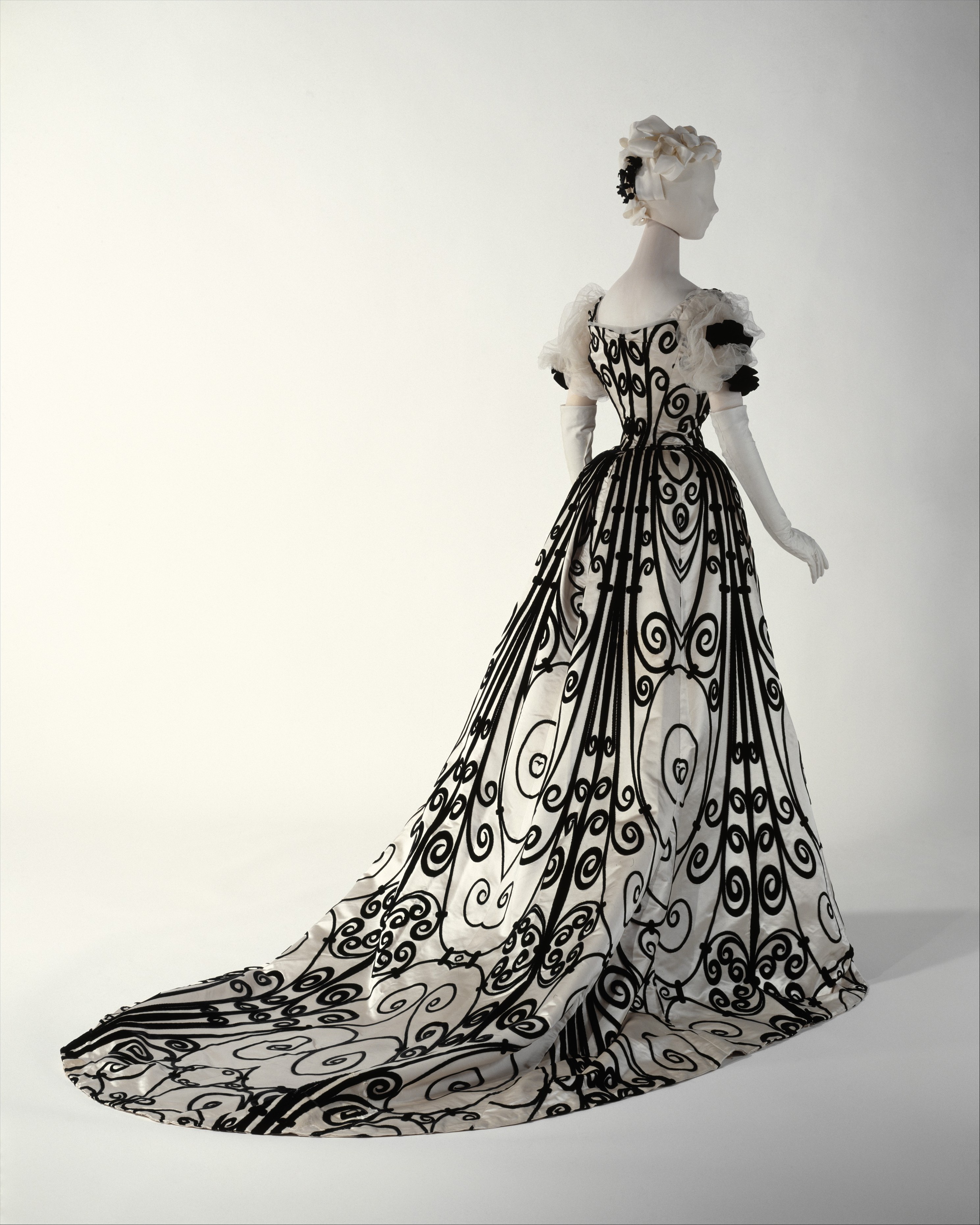 House of Worth silk evening dress from 1898 to 1900 with a pale embellished bodice, narrow waist, and richly patterned trained skirt.